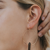 Close-up of an ear wearing a gold hoop earring with a black accent.