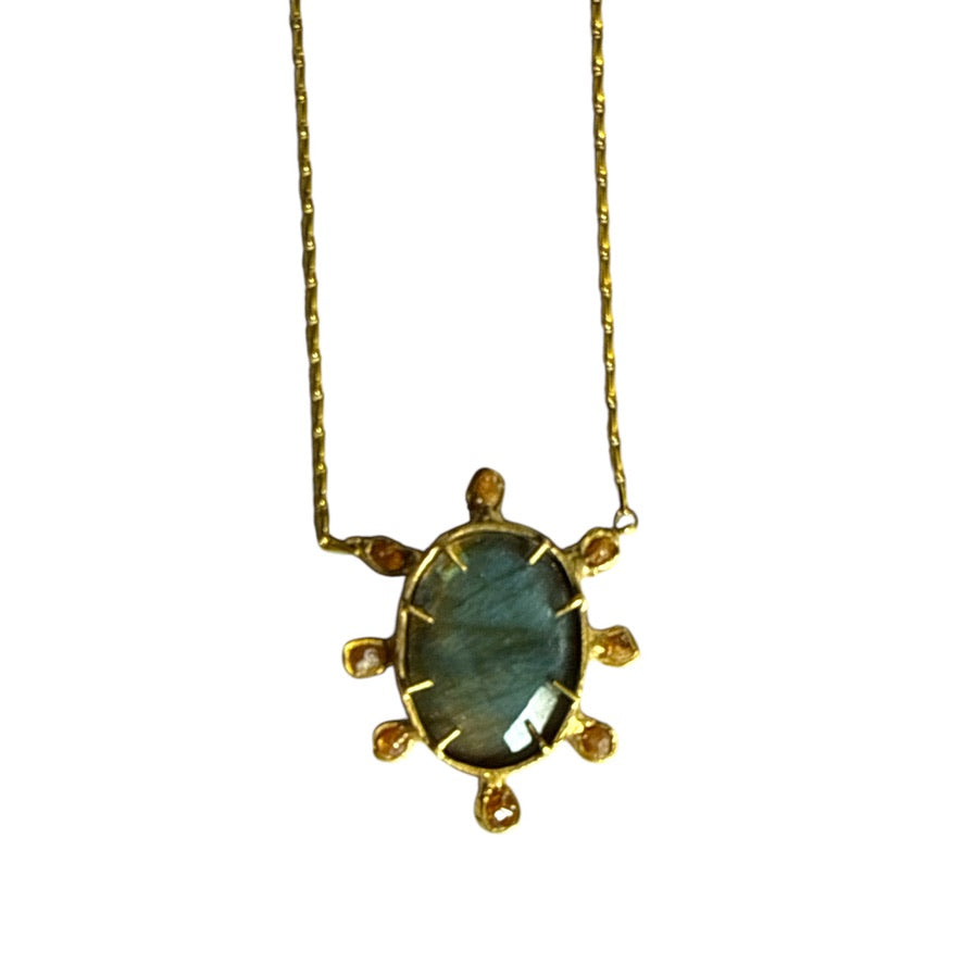A close up of a pendant necklace with a large oval shaped blue gemstone surrounded by 8 smaller beige gemstones on a white backgrouns