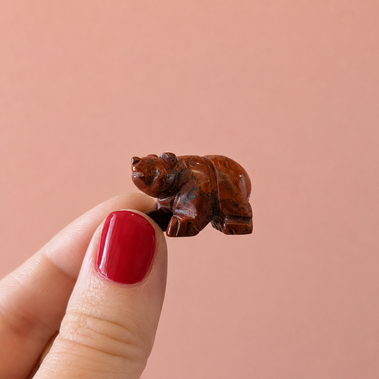 Small brown bear figurine held between fingers against a pink background