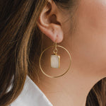 Gold hoop earring with a rectangular moonstone pendant in center, worn by a person
