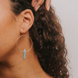 Woman with hoop earrings and a strapless top against a plain background