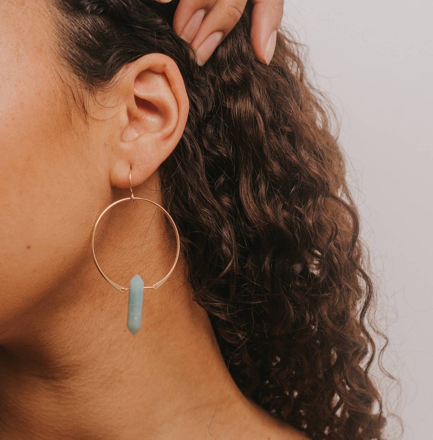 Woman with hoop earrings and a strapless top against a plain background