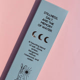 A light blue rectangular product box for Brass Earth incense sticks, photographed diagonally on a soft pink background. The box features black text describing a scent profile ('Stillness, Salt, and the Memory of Water') and a simple rabbit illustration.