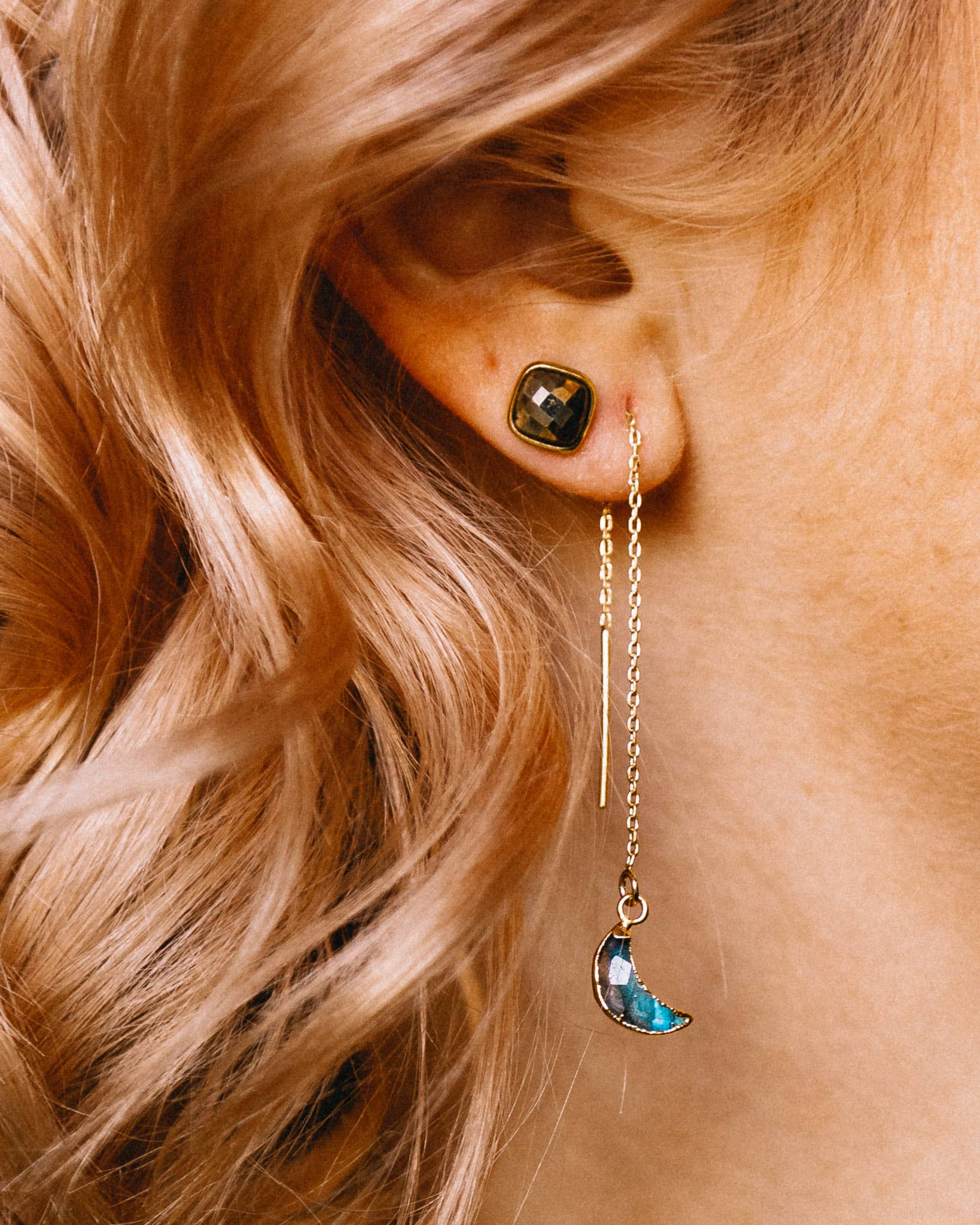 Close-up of an ear with a gold threader earring featuring a blue moon pendant.