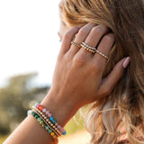 Close-up of a person wearing colorful beaded bracelets and rings outdoors.