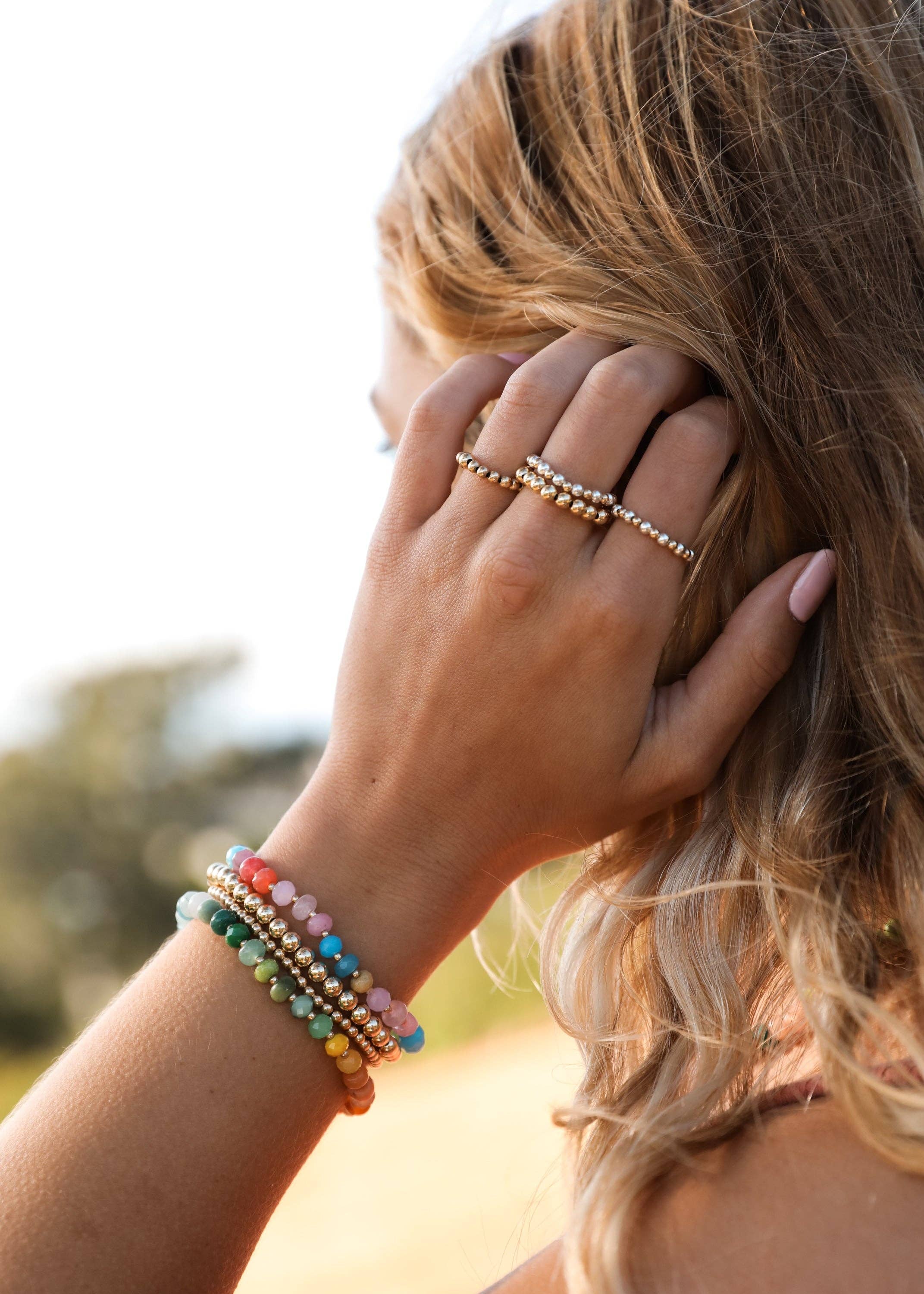 Close-up of a person wearing colorful beaded bracelets and rings outdoors.