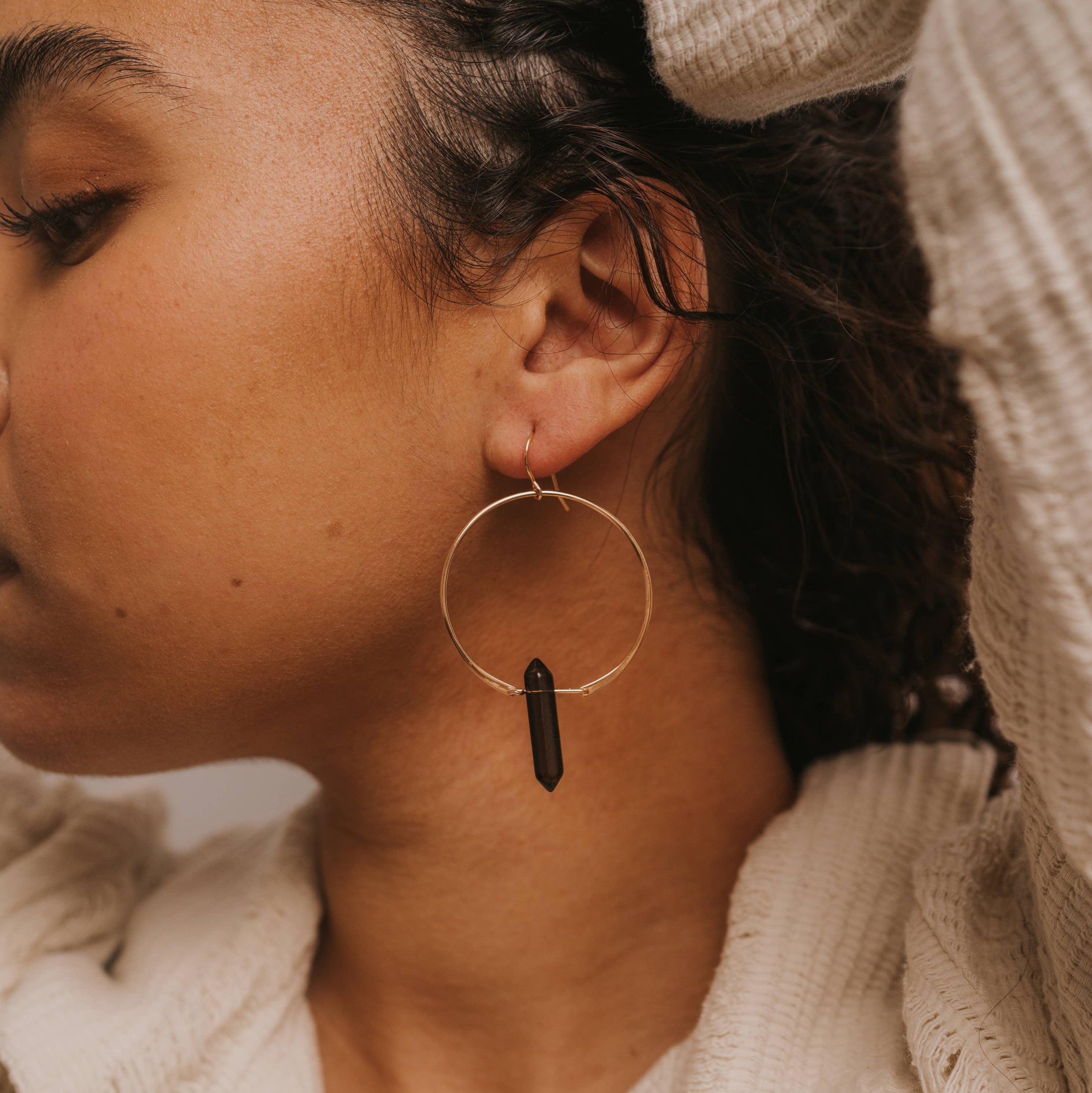 Close-up of a person wearing hoop earrings with a neutral background