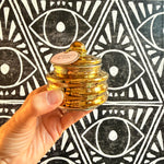 A hand holding a shiny gold vessel with Paddywax Cypress & Fir label against a black and white eye background