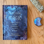 Book titled 'Practical Magic' on a wooden surface with crystals and a smudge stick.