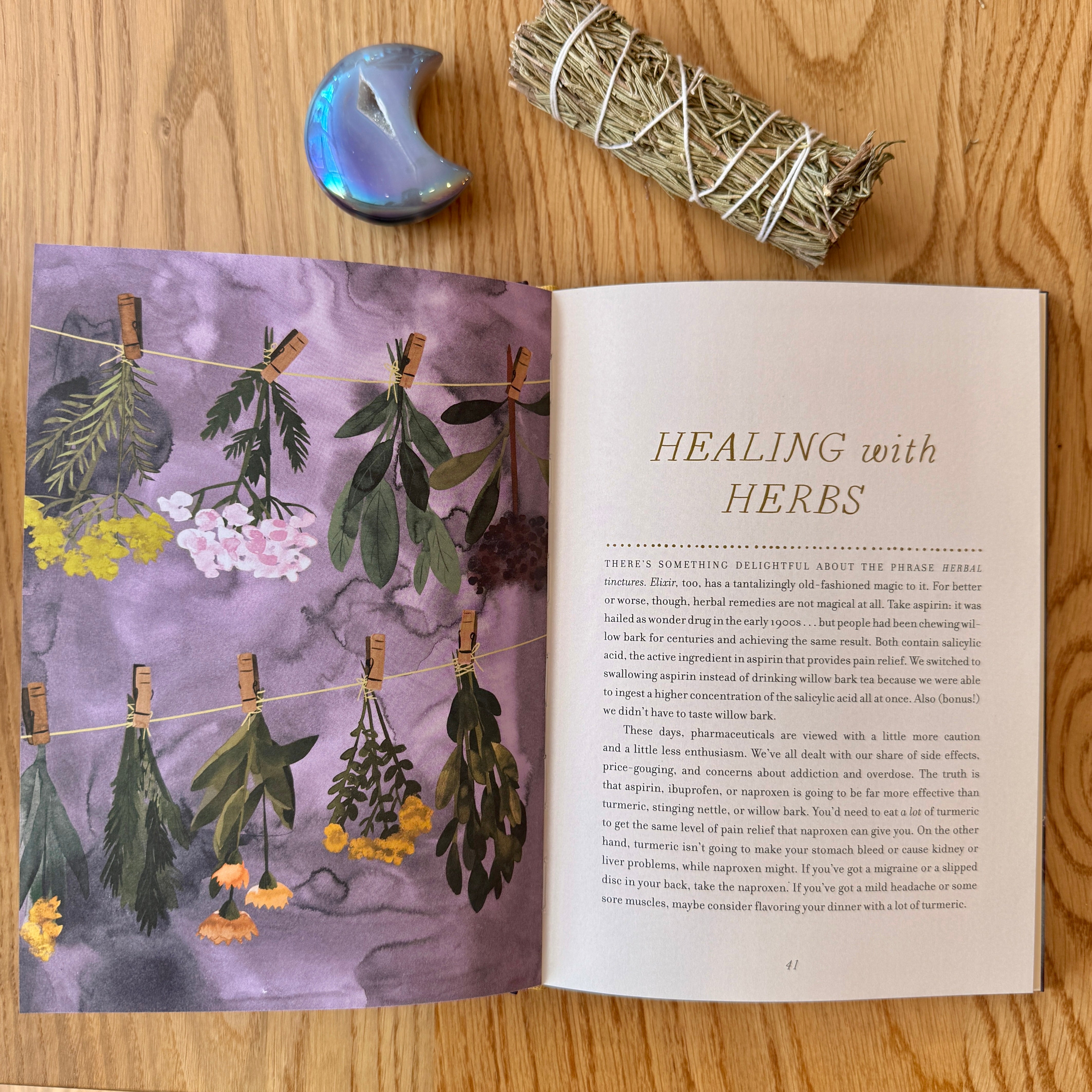 Open book titled 'Healing with Herbs' on a wooden surface with herbs and a crystal.