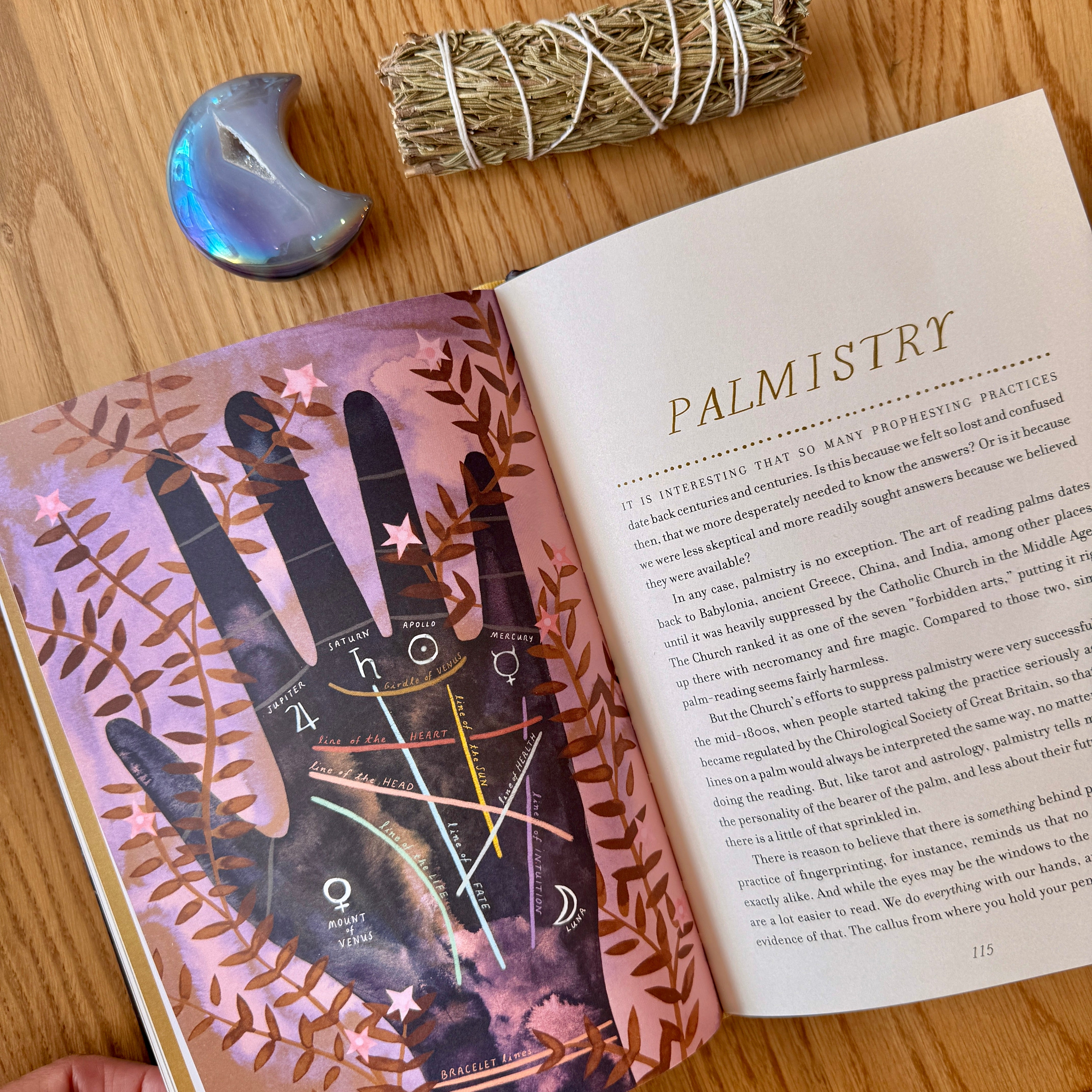 Open book on palmistry with a bundle of sage and ceramic moon phase on a wooden surface
