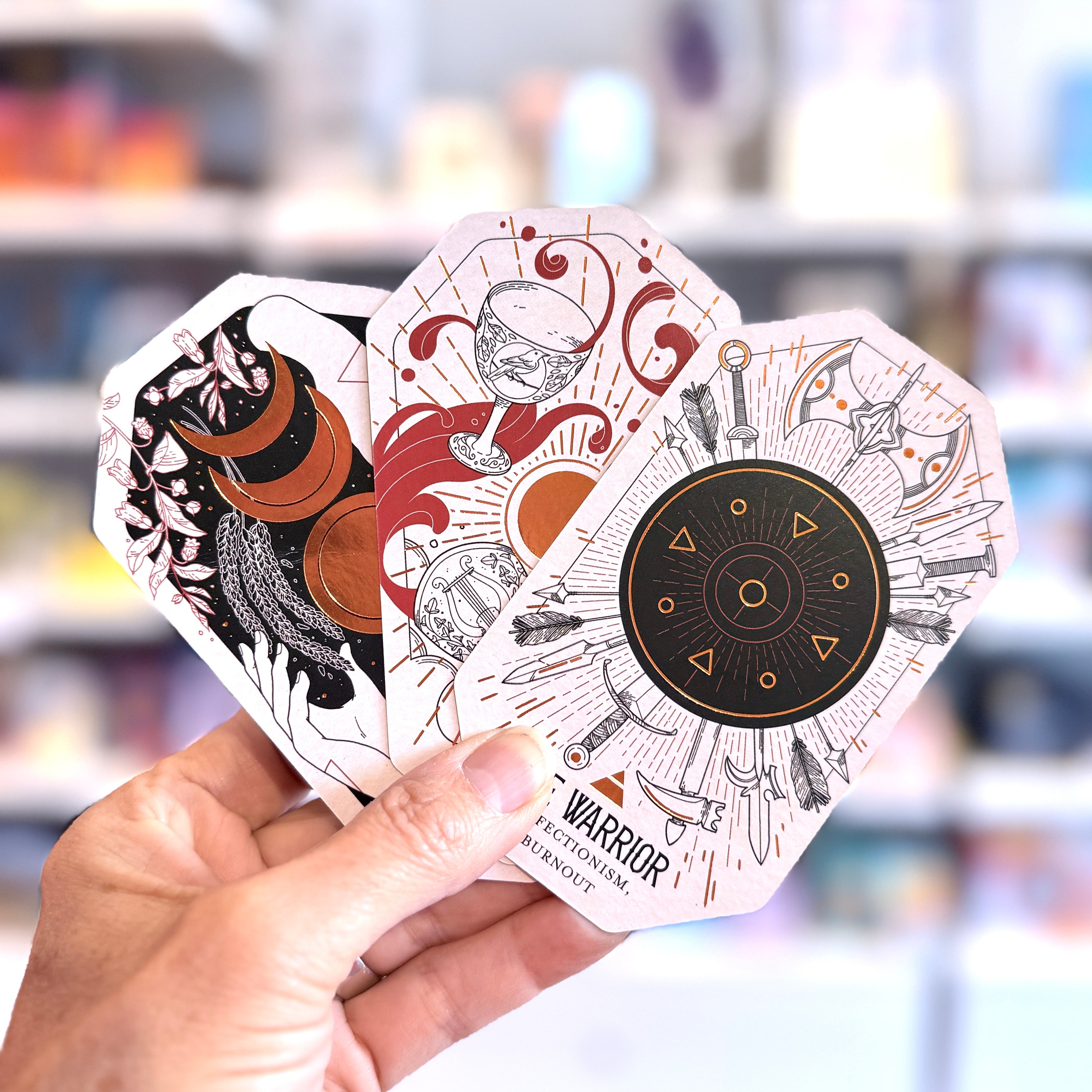 Hand holding three tarot cards with intricate designs against a blurred background