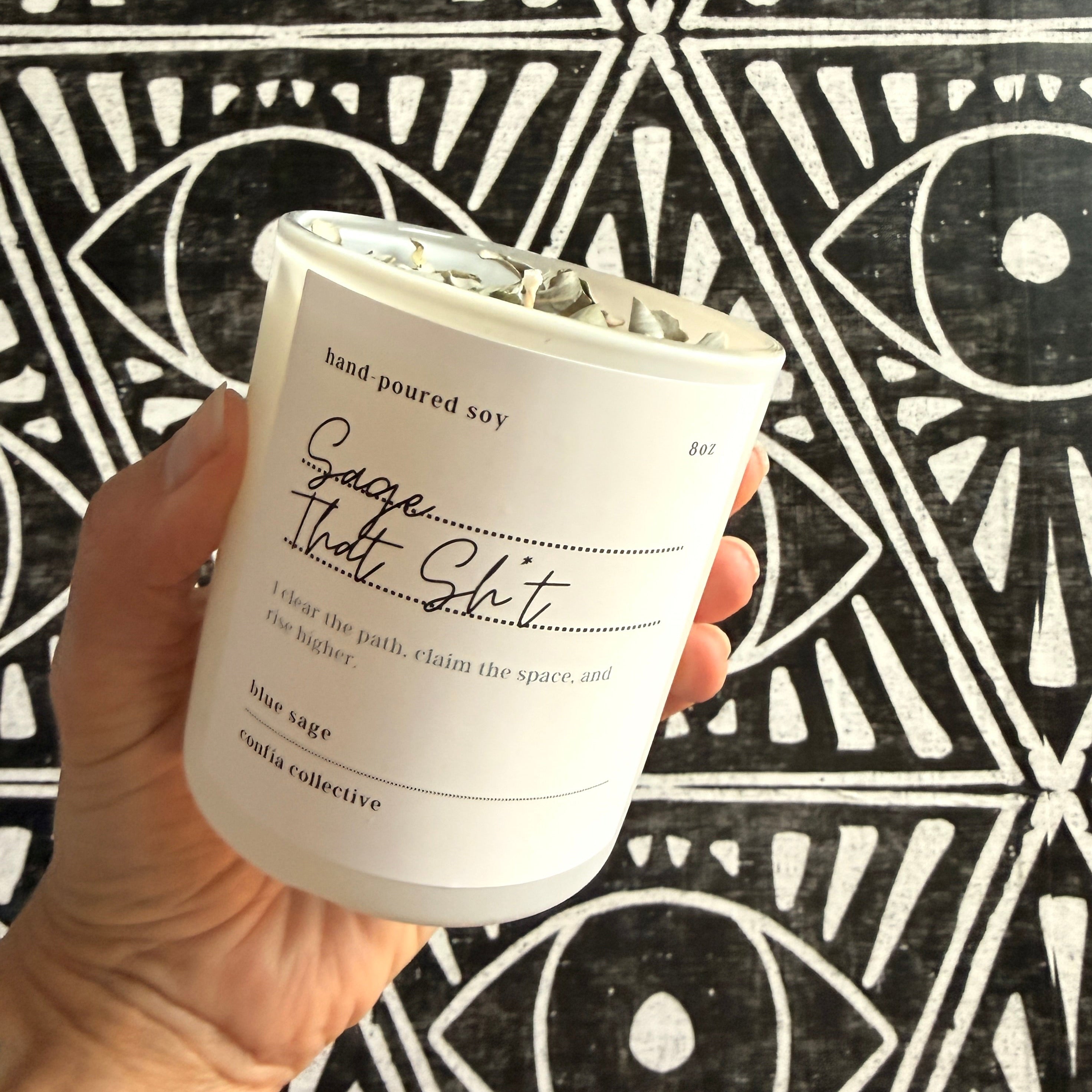 Hand holding a white candle with text against a black and white geometric patterned background