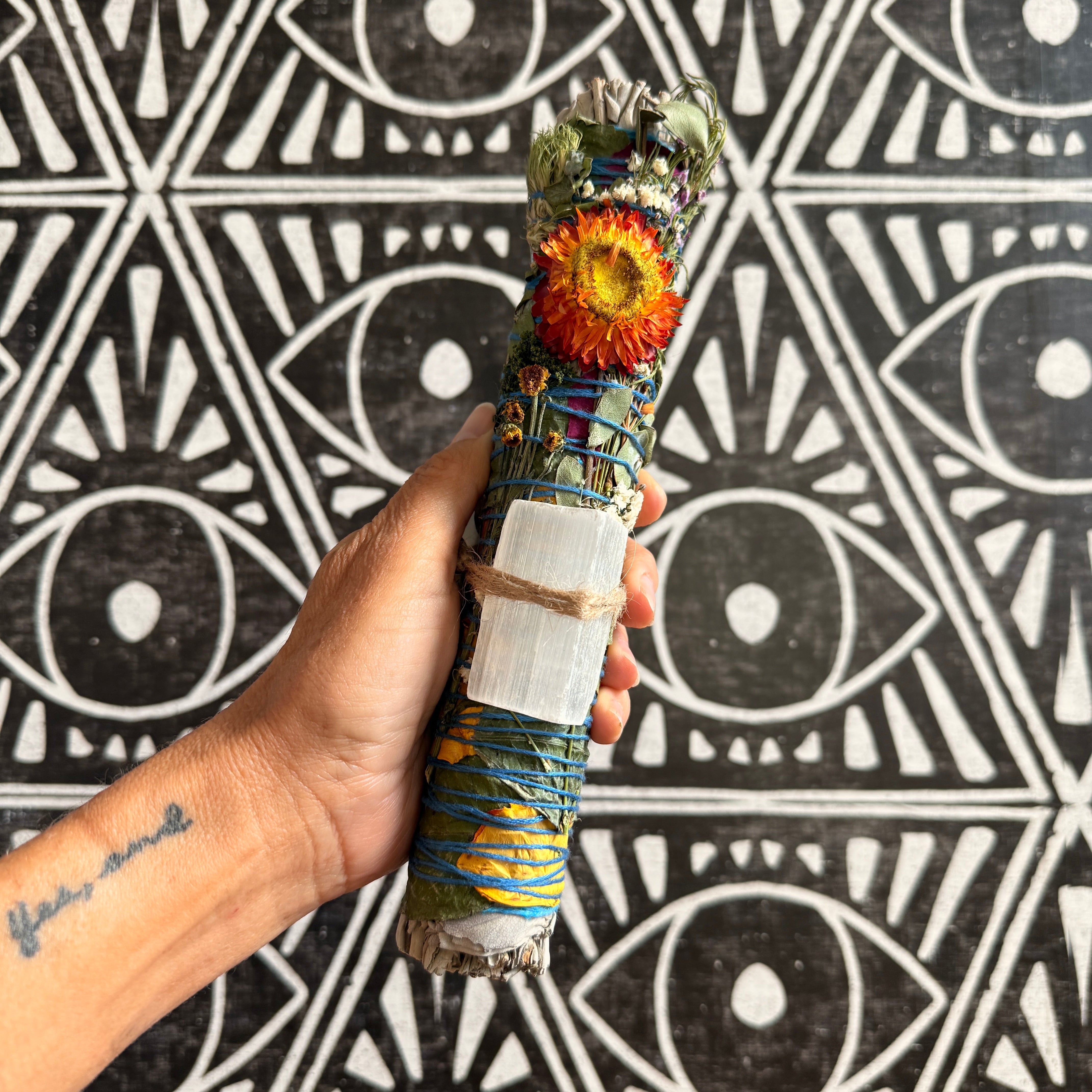 Hand holding a decorated smudge stick against a black and white patterned background