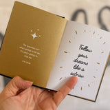 Open book with motivational quote on beige cover held by a hand