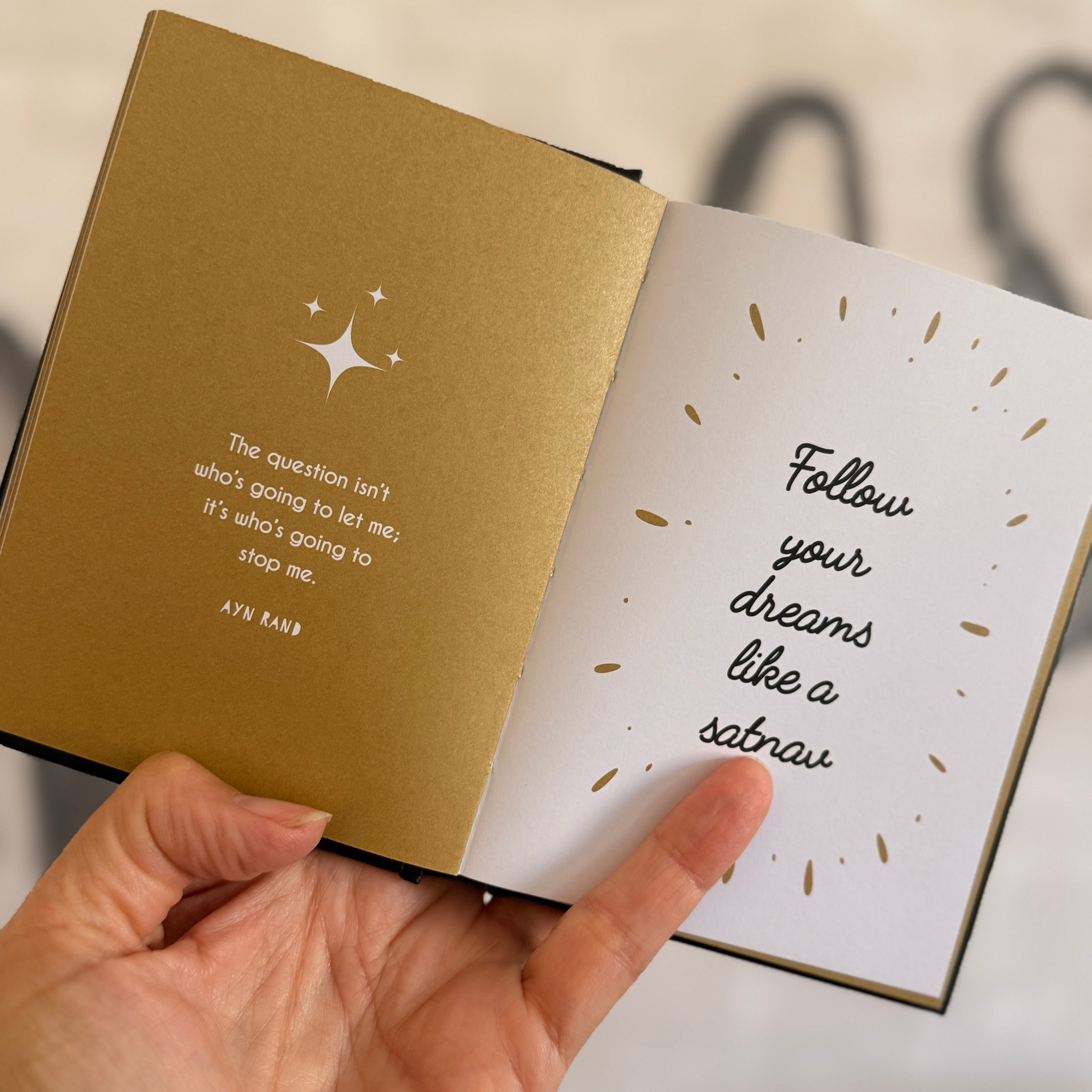 Open book with motivational quote on beige cover held by a hand