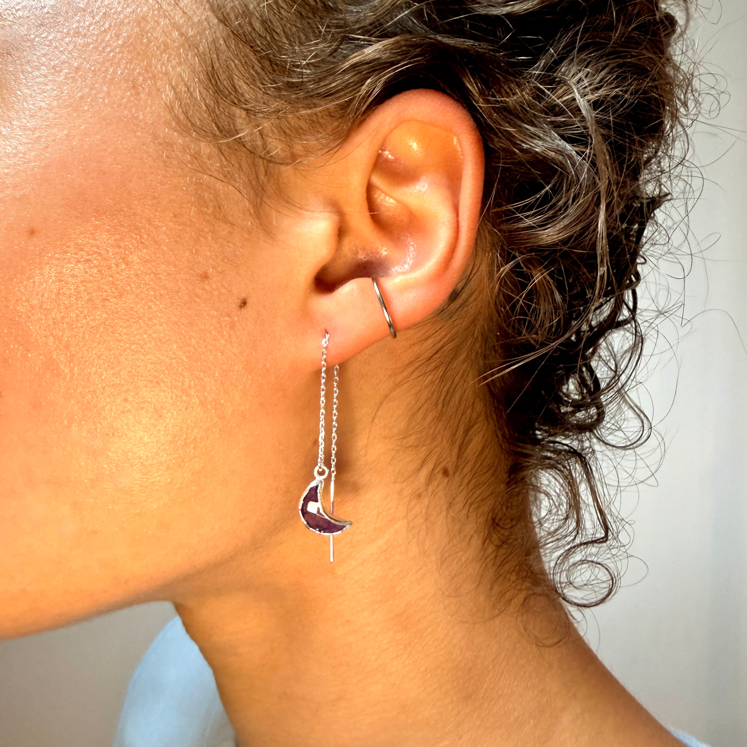 Close-up of an ear wearing a dangling crescent moon earring with a white background