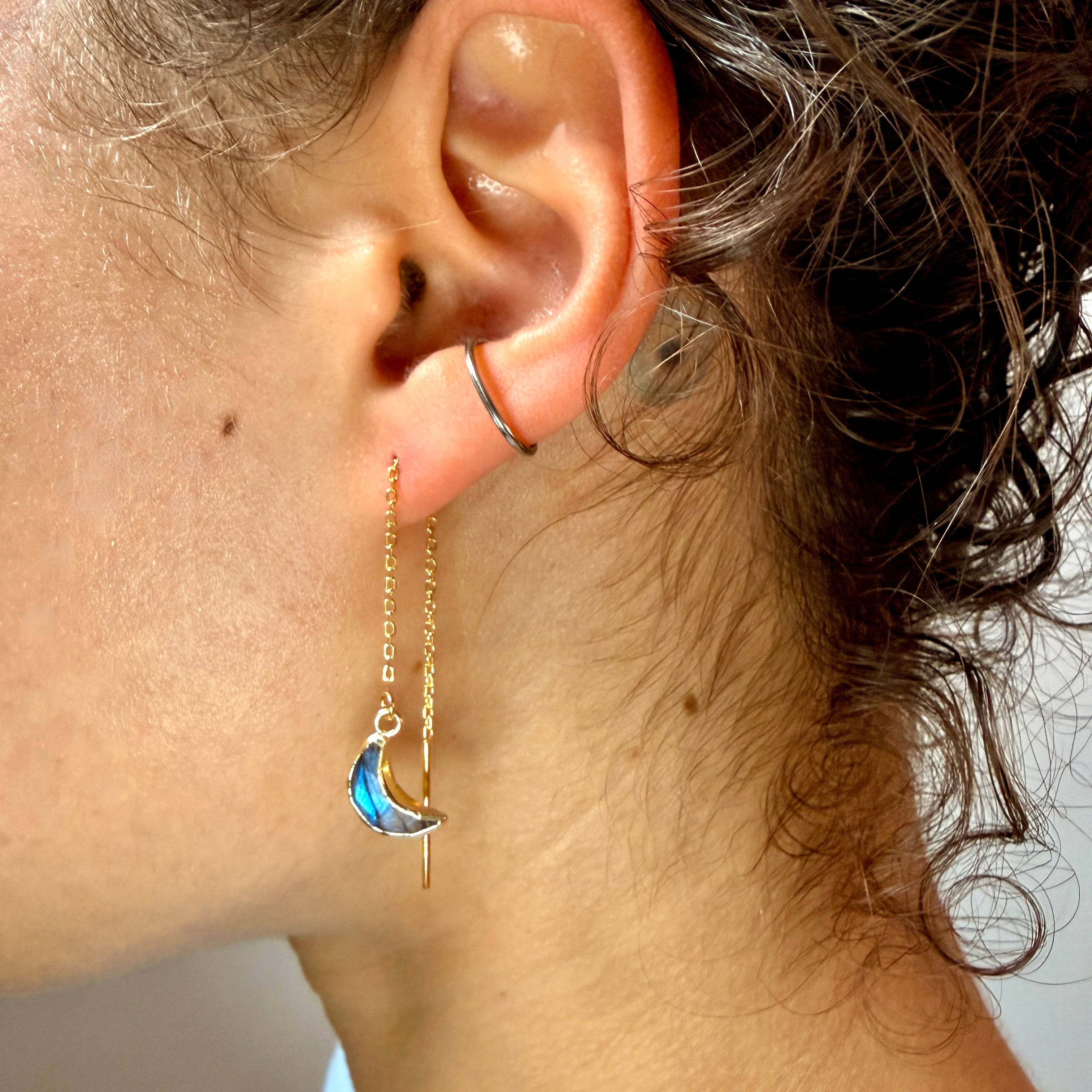 Woman wearing gold dropped earrings with a blue crescent moon shape