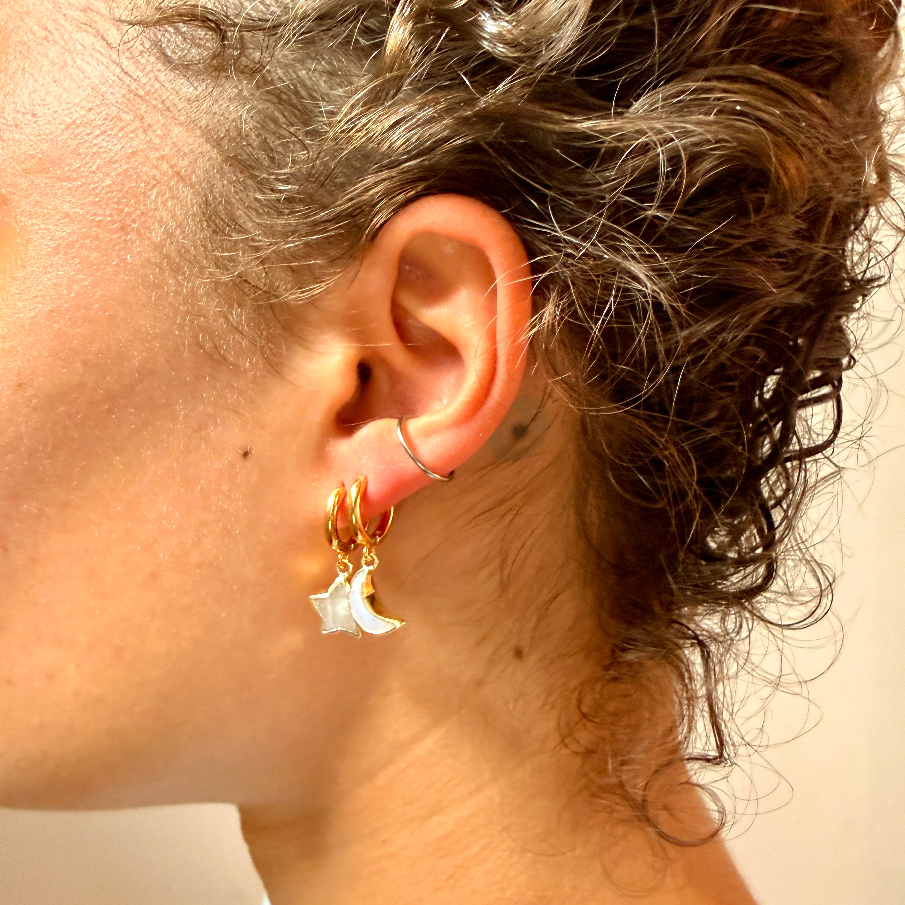 A woman wearing two gold earrings one a white star and the other a white moon