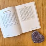 Open book on a wood surface next to a purple crystal