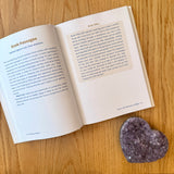 Open book on a wood surface next to a purple crystal