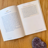 Open book with text on a wooden surface next to a crystal