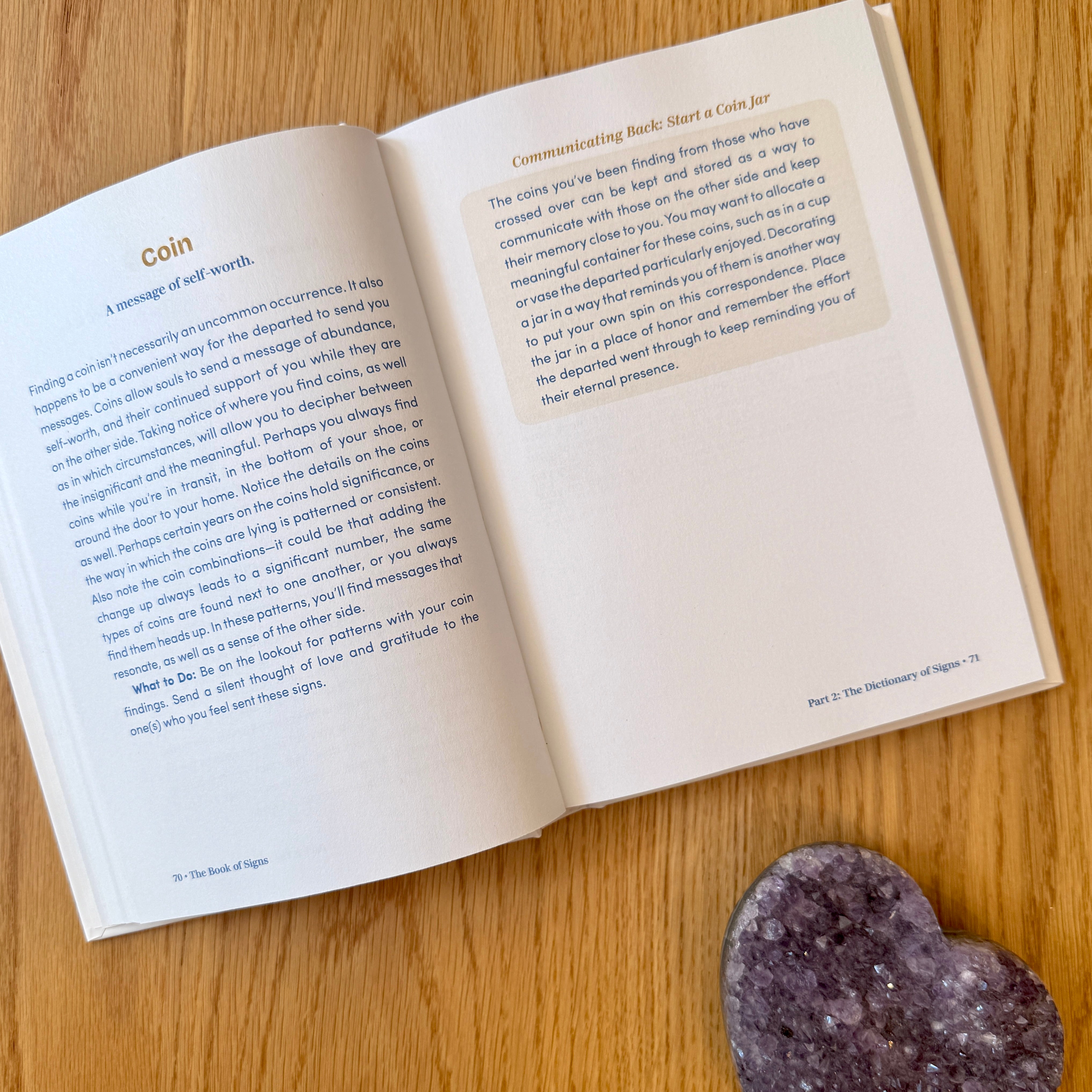 Open book with text on a wooden surface next to a crystal