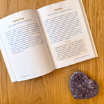 Open book on a wood surface with a purple crystal