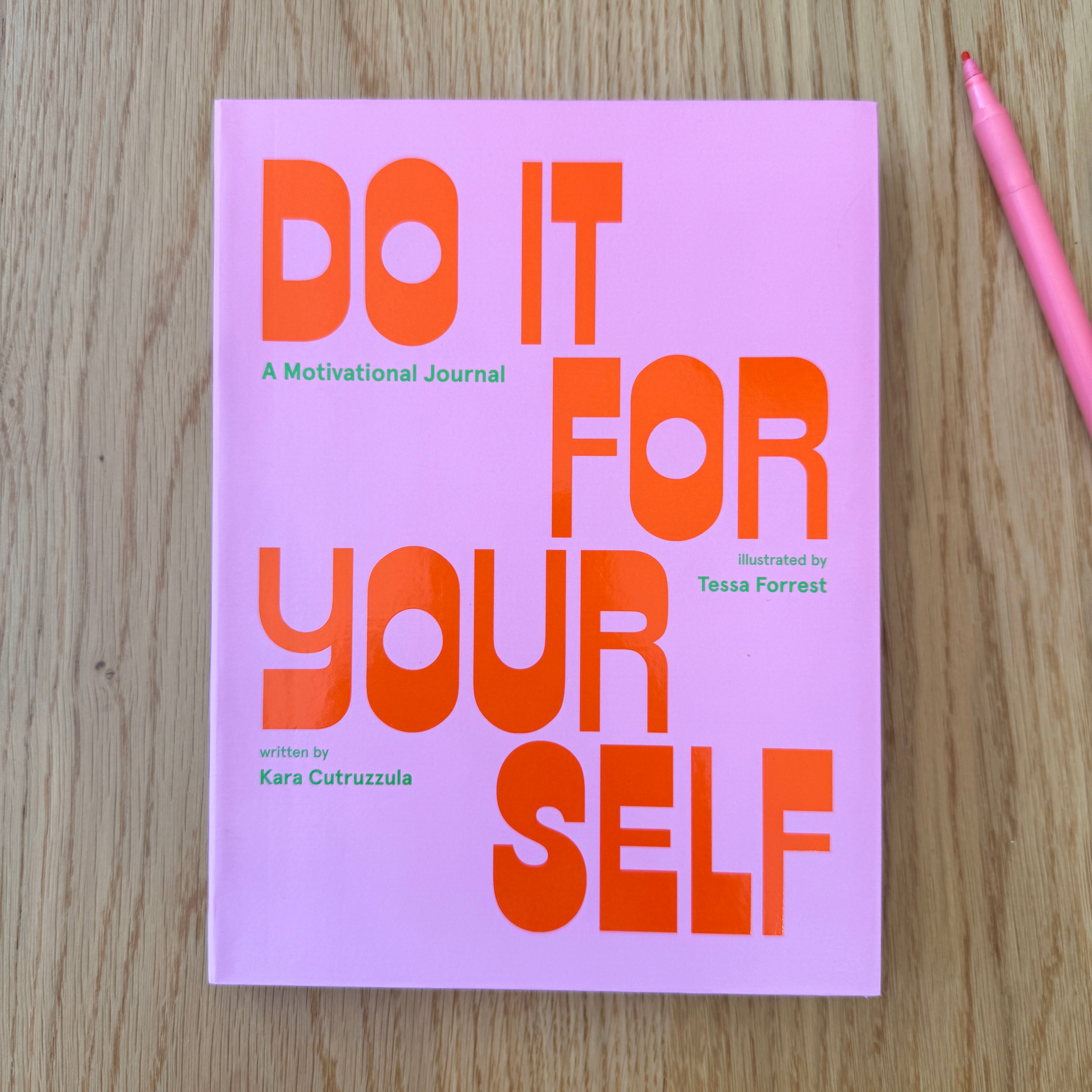 Bright pink book with Do It For Yourself on the cover on a wood surface