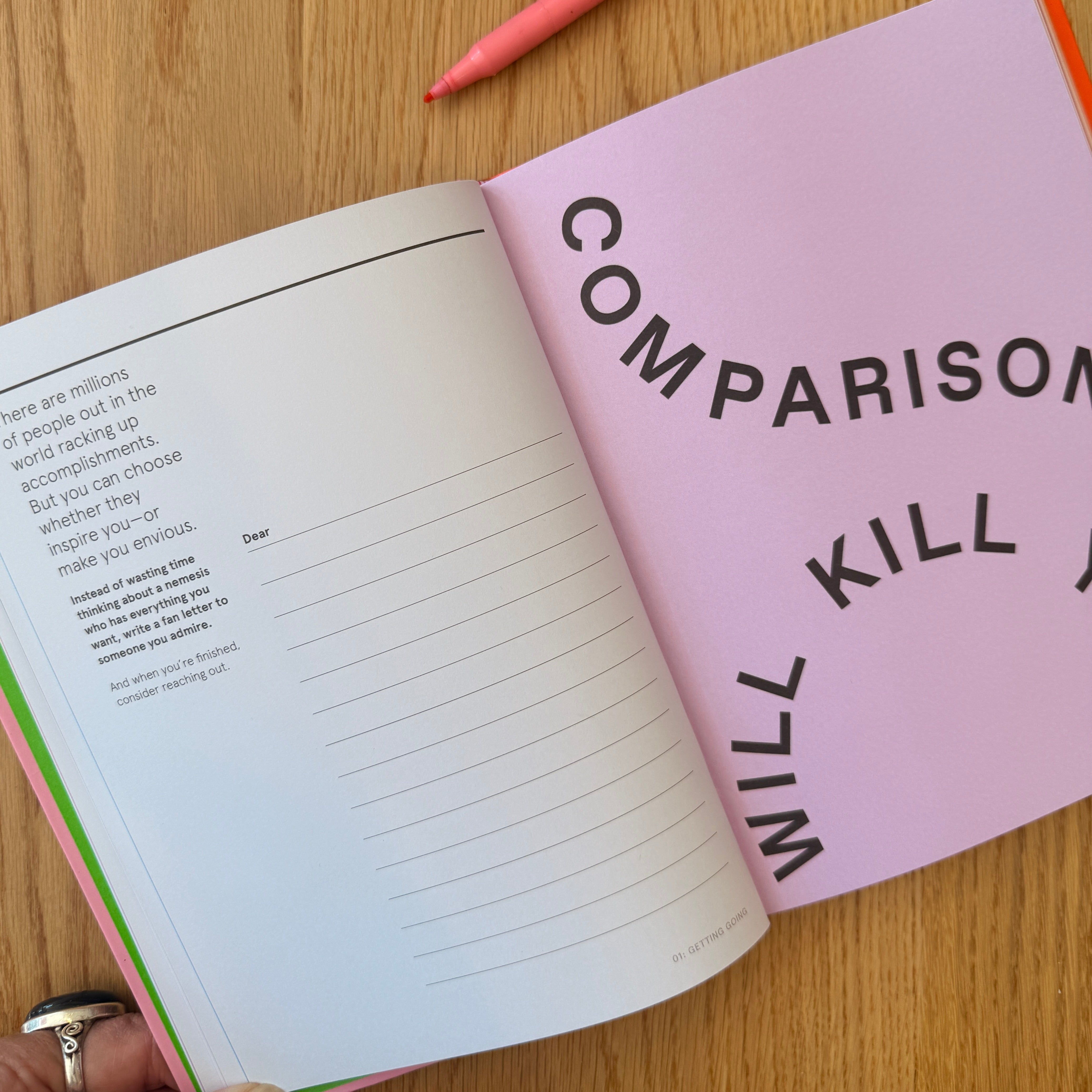 Open book with a pink page displaying the text 'Comparison will kill you' on a wooden surface.