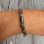 A close-up of a person's wrist wearing a beaded bracelet made of faceted dark gray stone beads, worn over a navy and white striped button-down shirt.