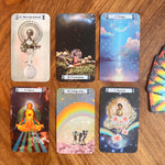 Six illustrated oracle or tarot-style cards arranged on a wooden surface, with a deck fanned out on the right. The cards feature colorful fantasy artwork and readable titles such as '5 Rebirth,' '10 Expansion,' '3 Change,' '8 Chakra,' '10 Conception,' and '7 Chastity.