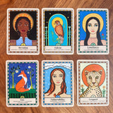 Six illustrated tarot-style cards arranged in two rows on a wooden surface. The cards feature stylized portraits and symbols with words such as Devotion, Falcon, Loneliness, Fox, Vulnerability, and Leopard.