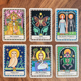 Six illustrated oracle cards arranged in a 2x3 grid on a wooden surface. The cards feature fantasy and spiritual imagery including a council of animals, a moth, a skeleton, a white owl, a swan, and a green creature, with titles such as The Council, The Moth, The Death Whisperer, The White Owl, The Messenger, and Scab.