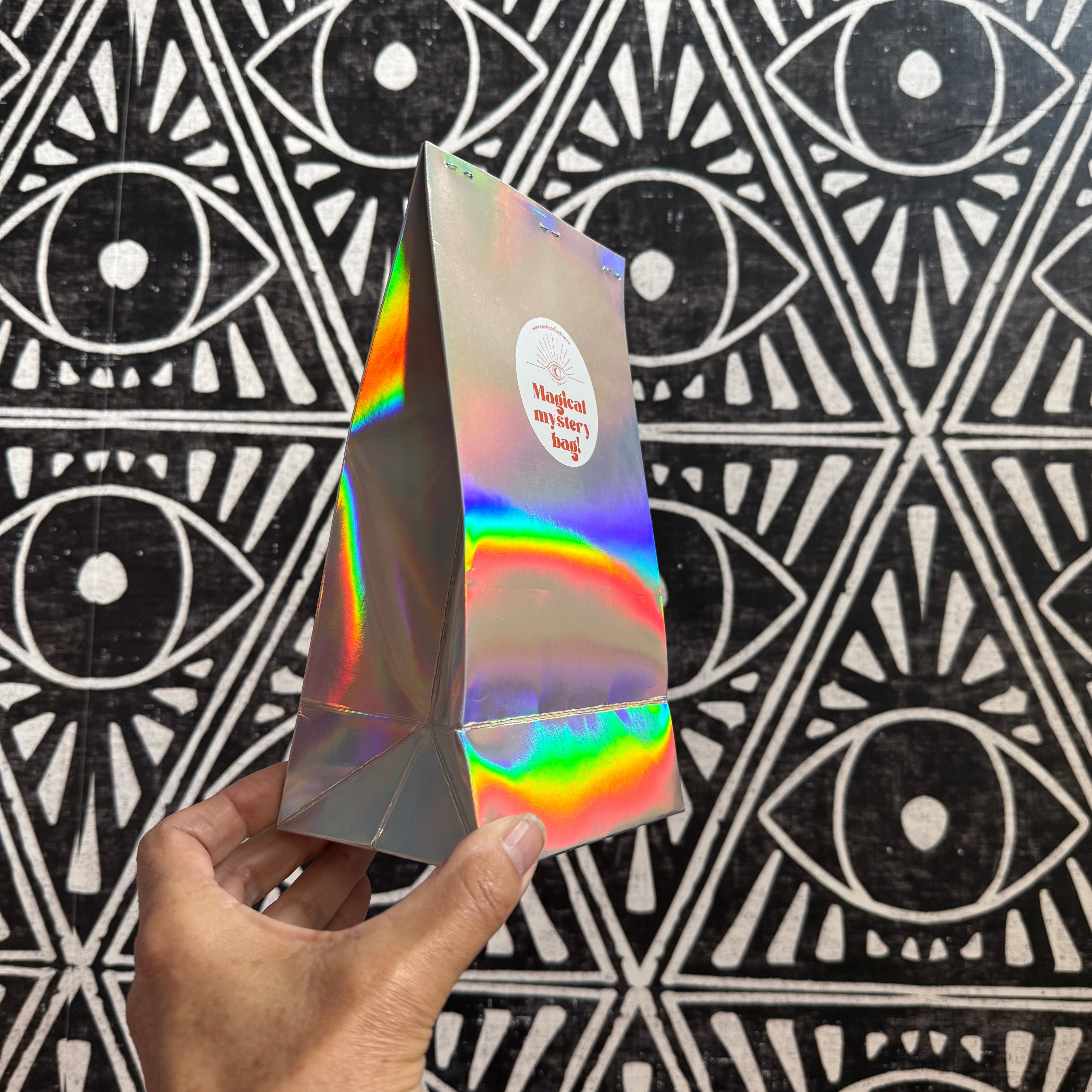 Hand holding a magical mystery iridescent bag against a black and white geometric patterned background