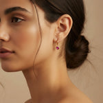 Close-up of a woman wearing a gold earring with a pink gemstone on a beige background