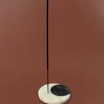 A minimalist incense holder made of a white marble base with a black semicircle on one side, holding a single vertical black incense stick, set against a solid terracotta background.