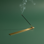 Gold incense burner with a smoking incense stick on a green background