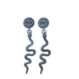 Pair of silver eye-shaped earrings with tassels on a blue card, placed on a stone surface.