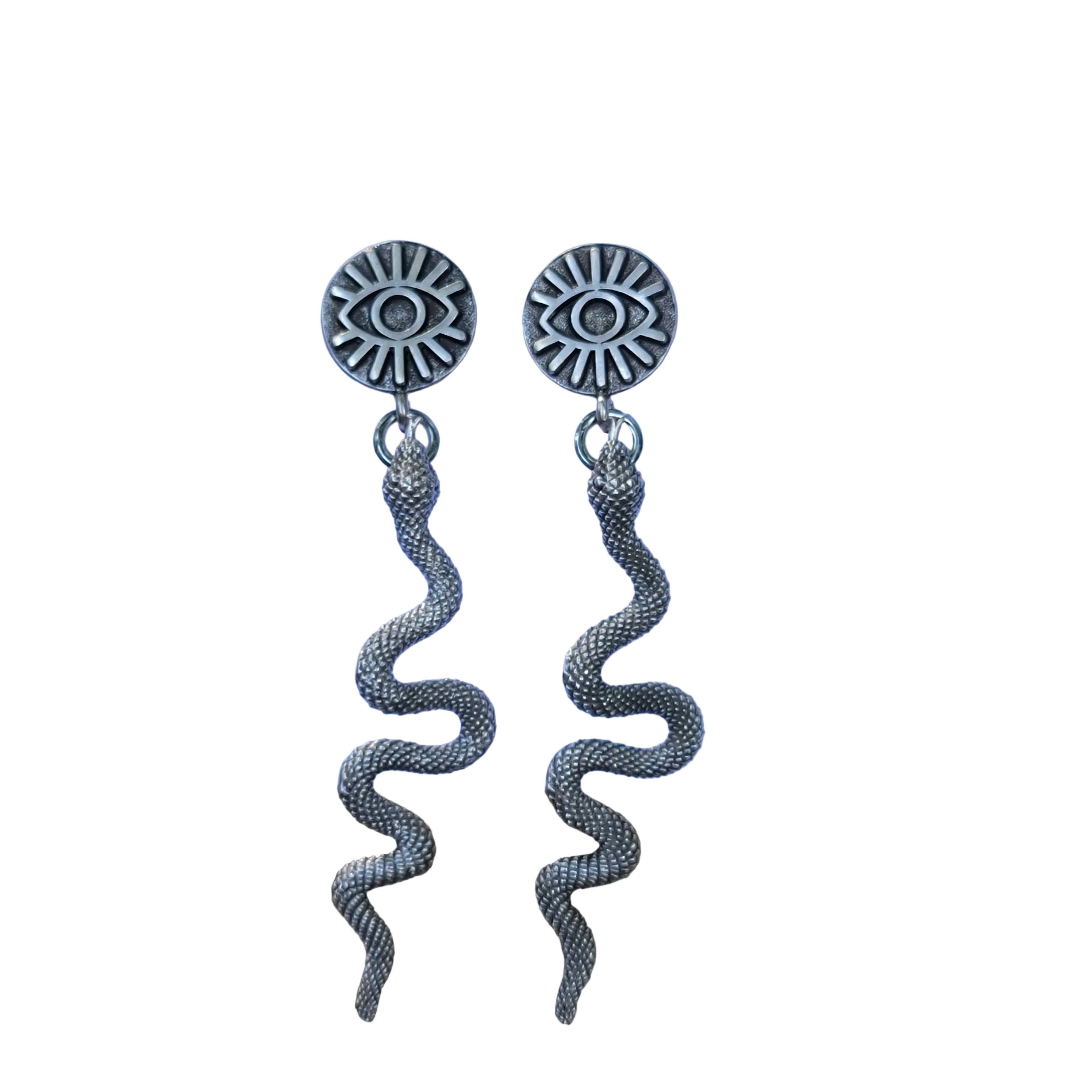 Pair of silver eye-shaped earrings with tassels on a blue card, placed on a stone surface.