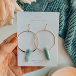 Jewelry card with hoop earrings featuring amazonite stones, held over a soft fabric background.