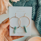 Jewelry card with hoop earrings featuring amazonite stones, held over a soft fabric background.