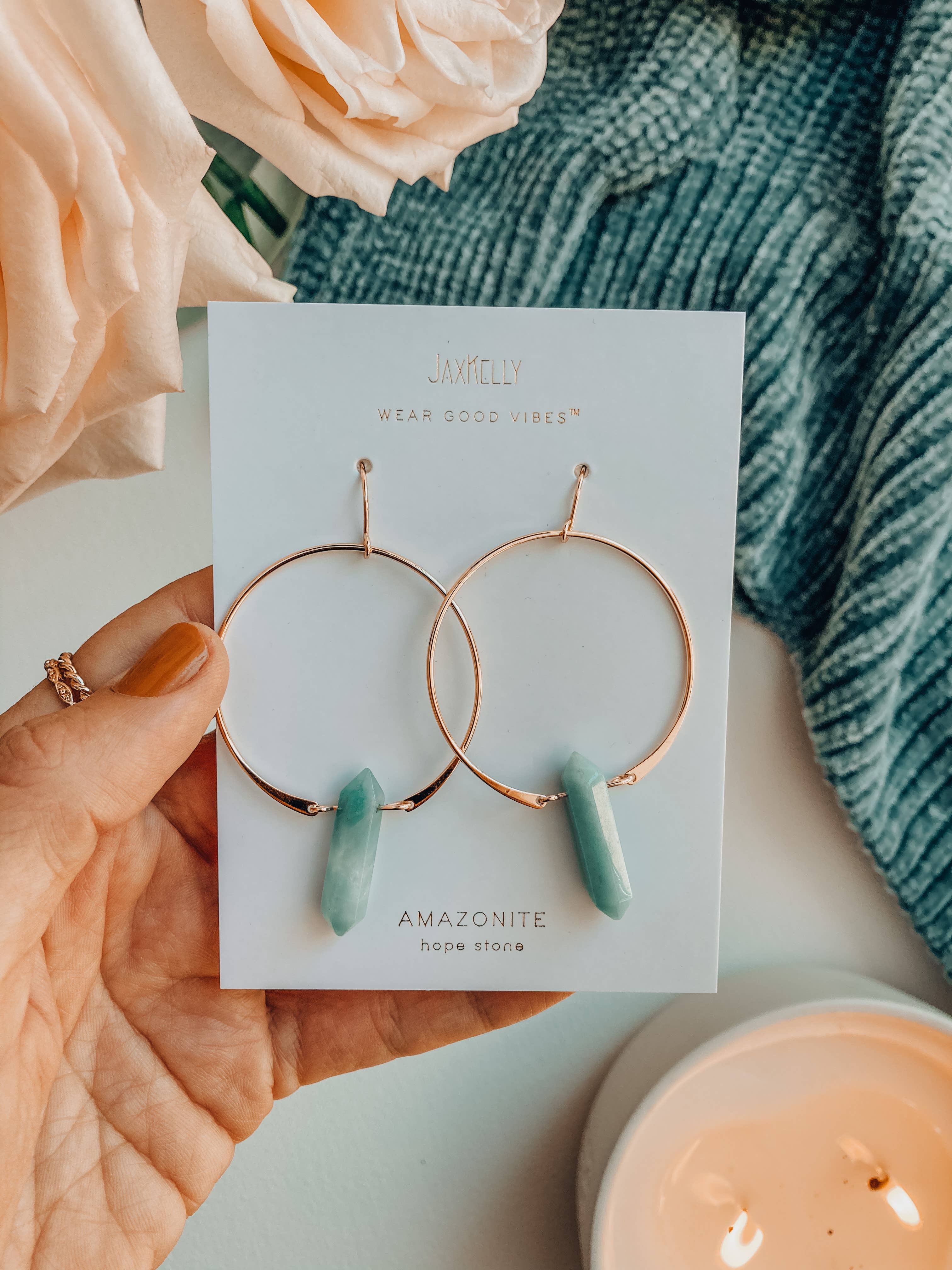 Jewelry card with hoop earrings featuring amazonite stones, held over a soft fabric background.