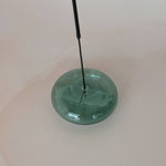 Green glass object with a long black rod on a white background