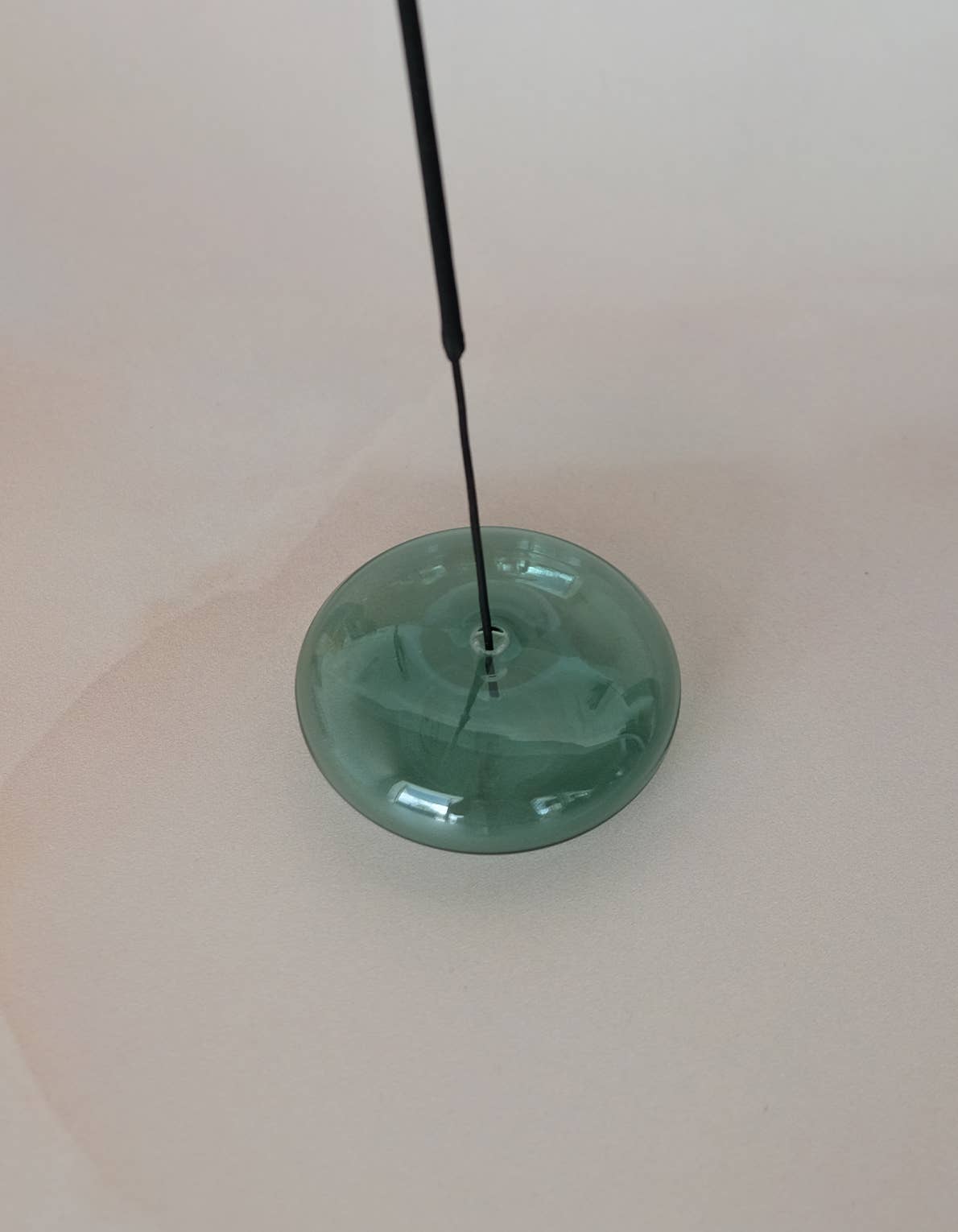 Green glass object with a long black rod on a white background