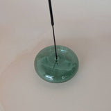 Green glass object with a long black rod on a white background