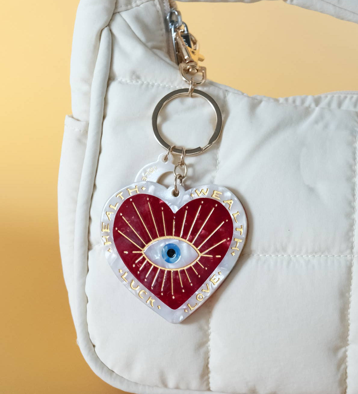 Heart-shaped keychain with an eye design on a white bag against a yellow background