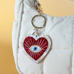 Heart-shaped keychain with an eye design on a white bag against a yellow background