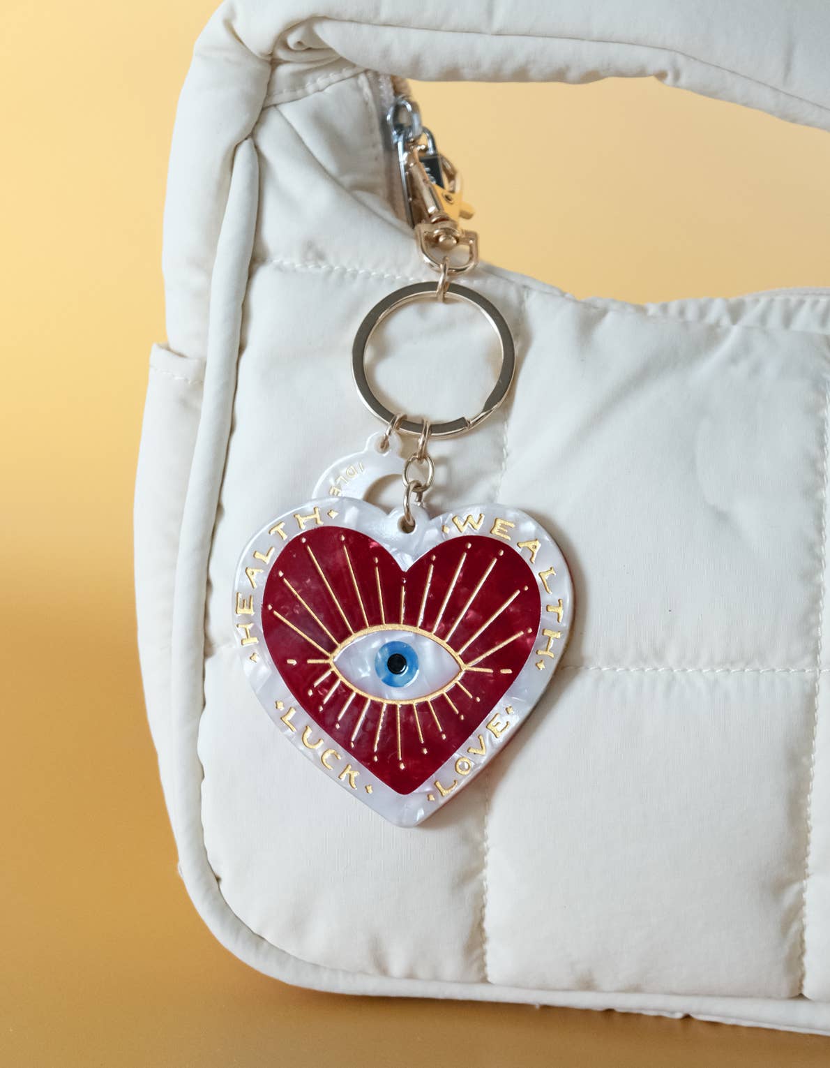 Heart-shaped keychain with an eye design on a white bag against a yellow background
