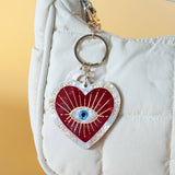 Heart-shaped keychain with an eye design on a white bag against a yellow background